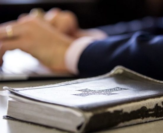 A bible with hands in the background.