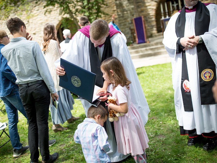 Two kids looking at a graduate's diploma.